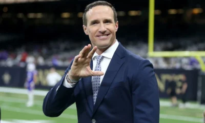 Drew Brees in a suit and tie holding his hand up