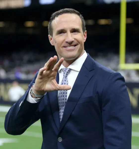 Drew Brees in a suit and tie holding his hand up