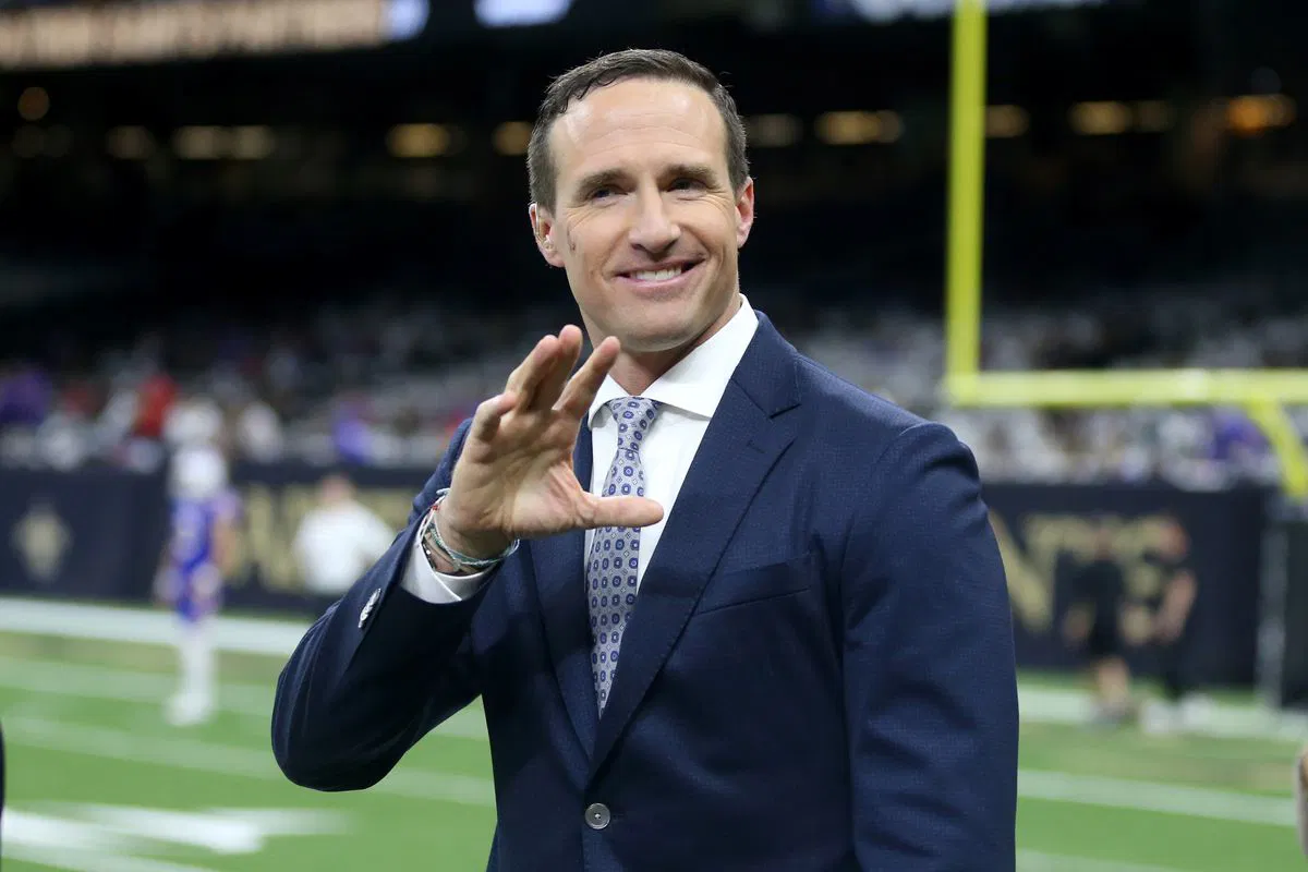 Drew Brees in a suit and tie holding his hand up